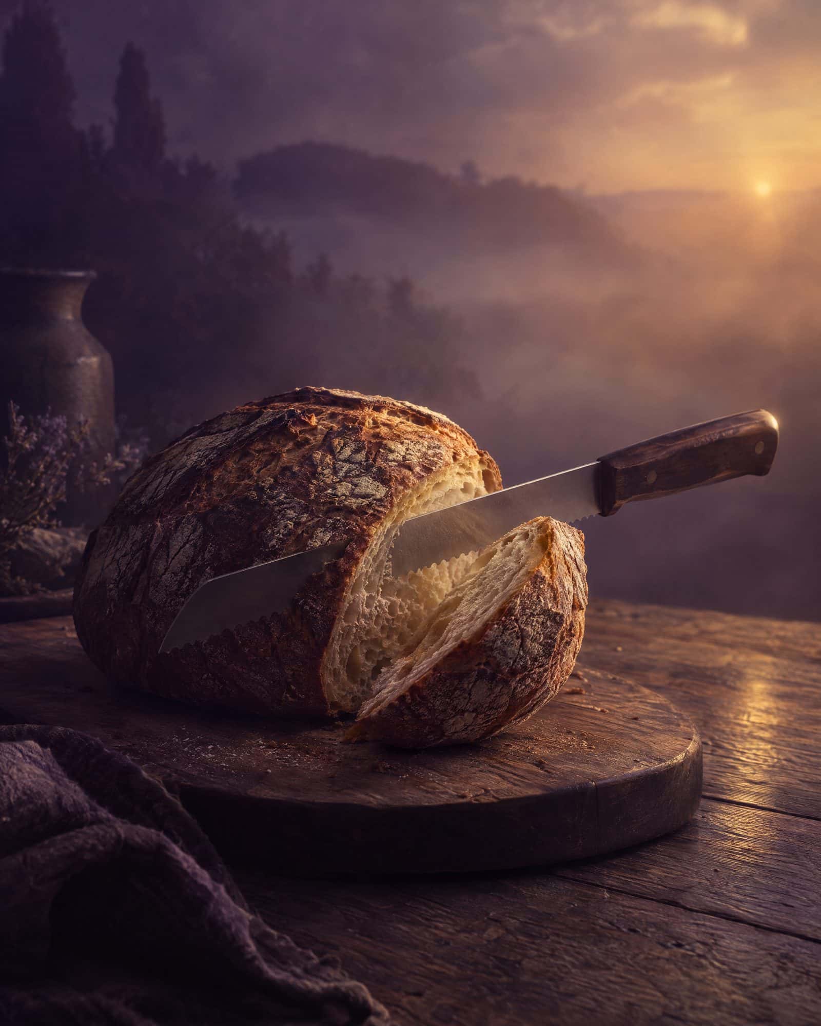 A loaf of bread on a board, a knife cutting through it.