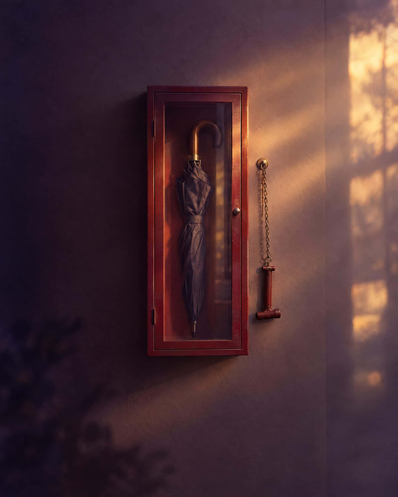 A glass-fronted emergency cabinet holding an ordinary umbrella, a small hammer beside it